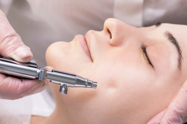 A person receives a facial treatment with a skin care device while lying down, administered by someone wearing gloves.